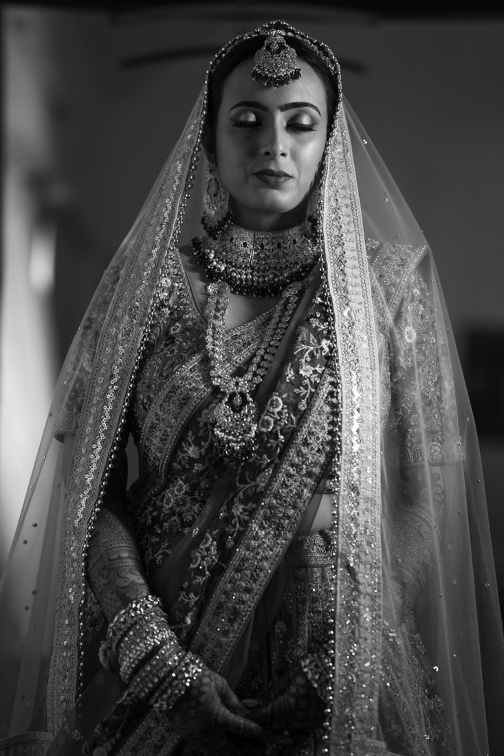 A bride in a jewelled veil, eyes closed, in black and white