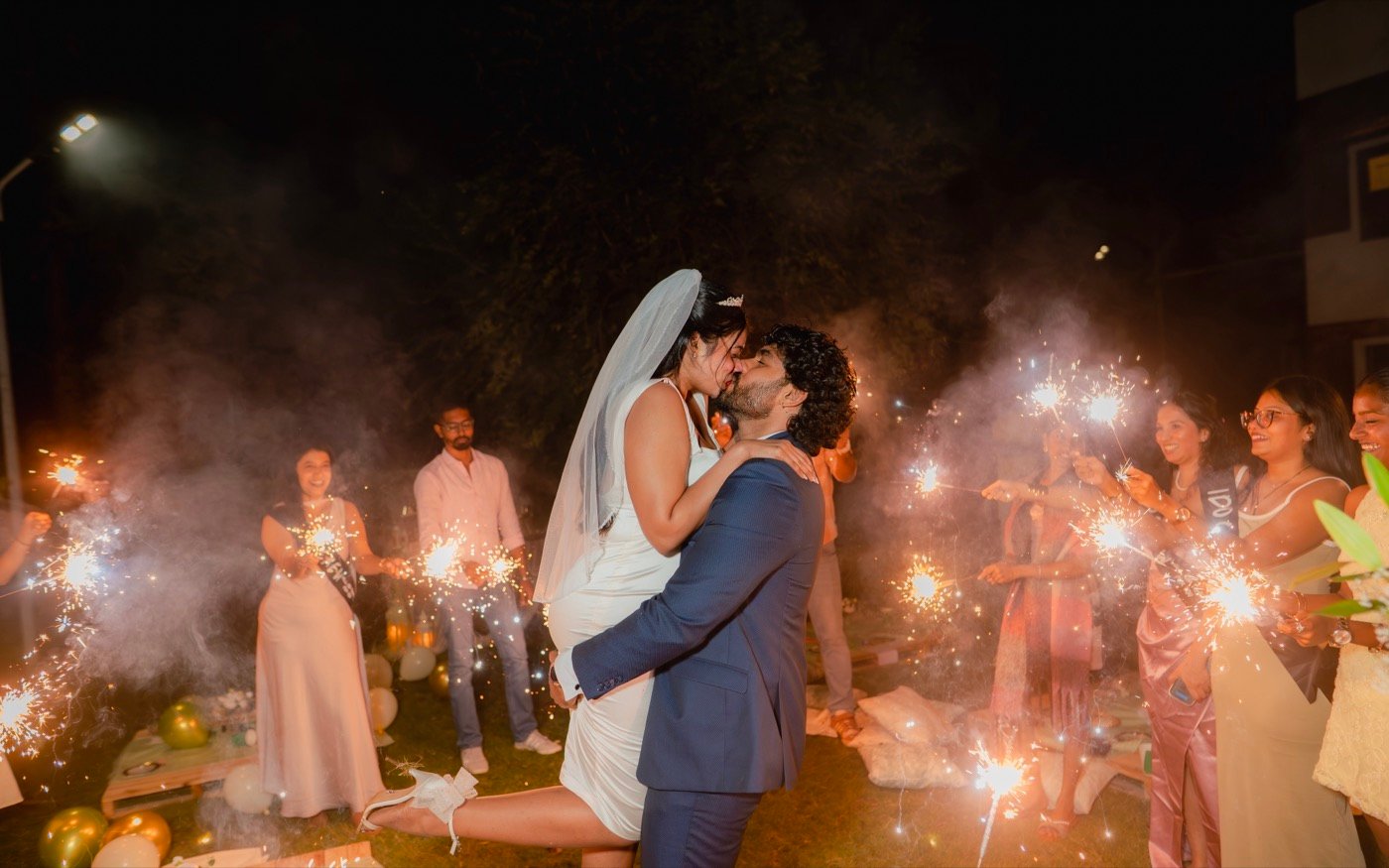 A couple kissing at night as guests light sparklers around them