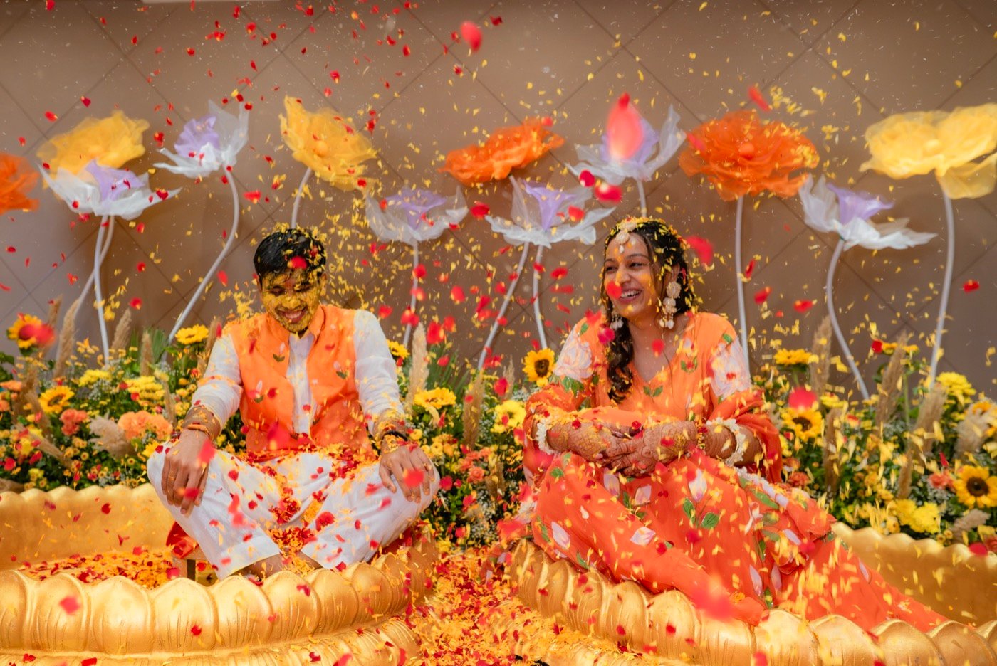 A couple seated in a flower-filled haldi setting as petals fall