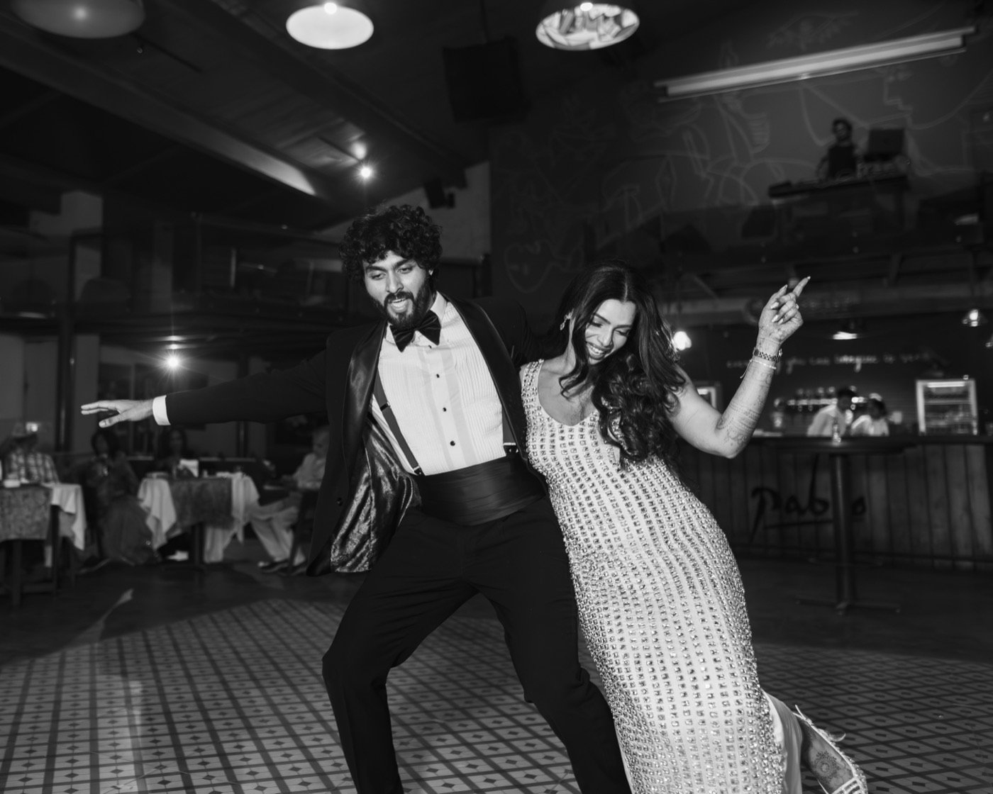 A couple dancing across a chequered floor, in black and white