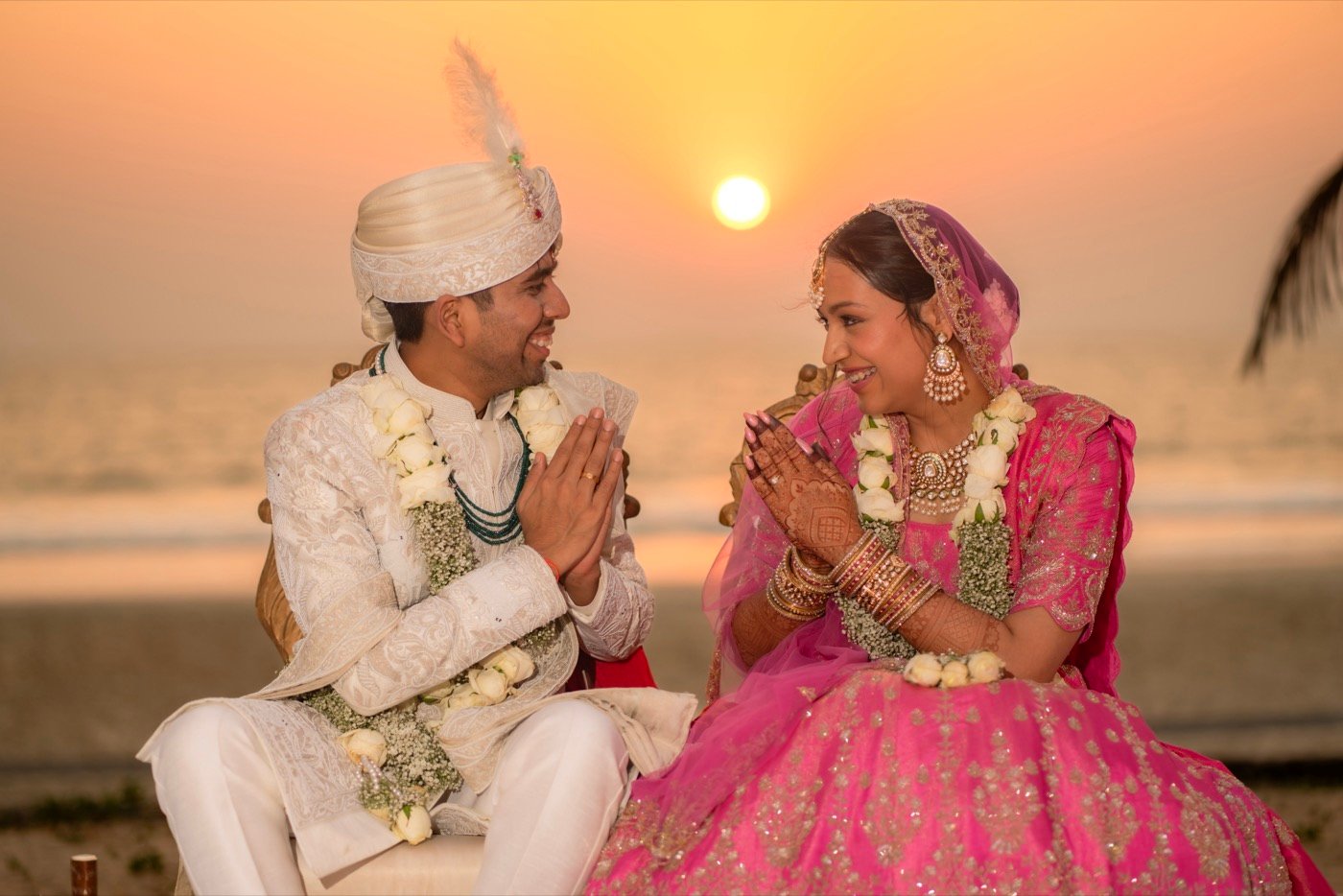 A bride and groom with folded hands at sunset by the sea