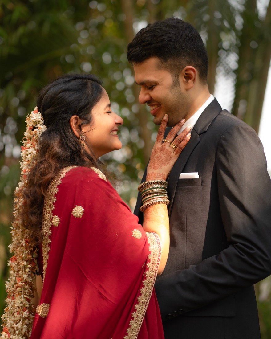 A bride in red touching the groom's face in a garden