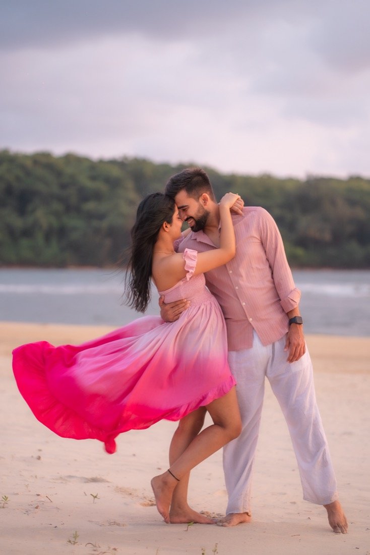A couple on a beach, the bride's pink dress lifting in the wind