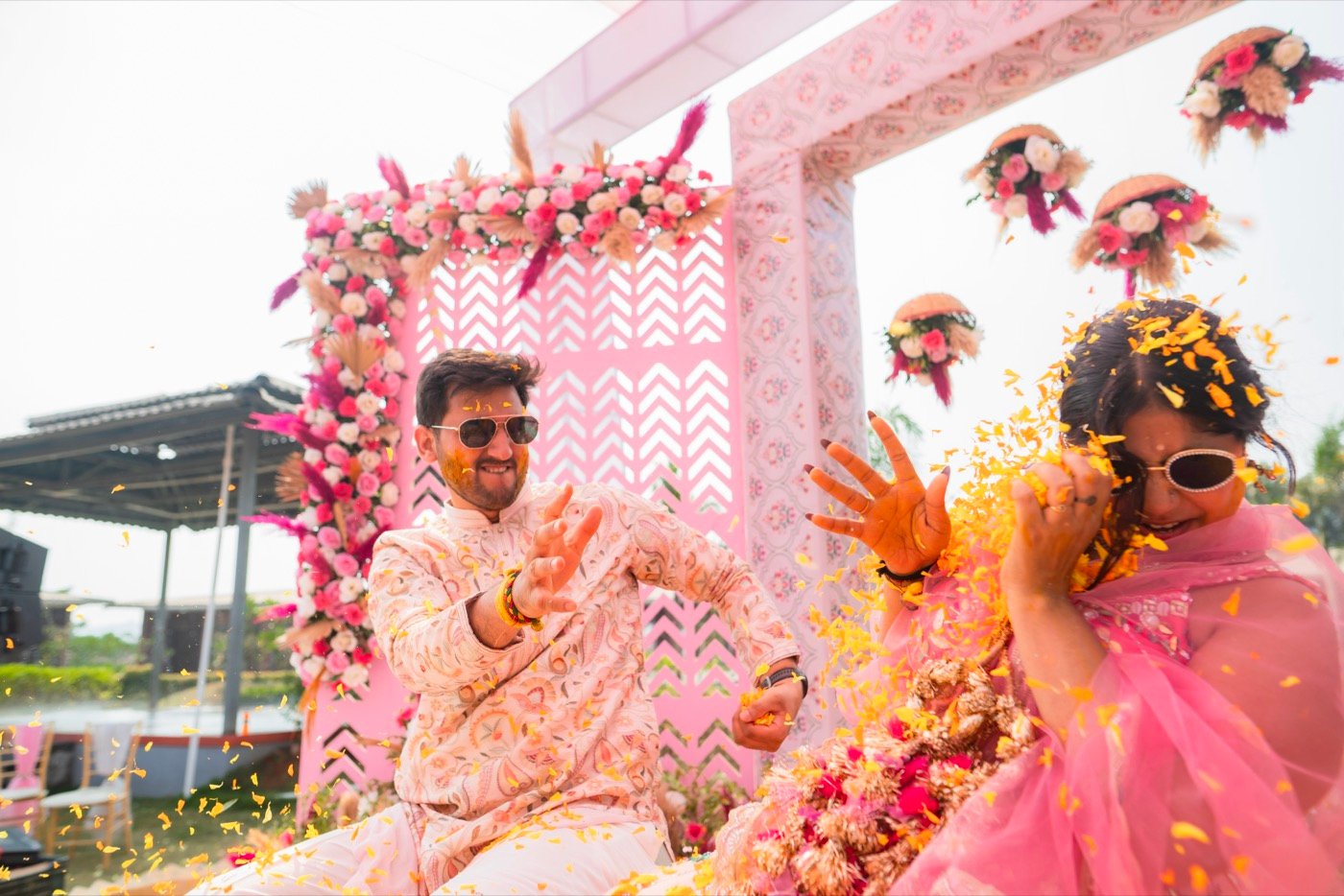 A couple laughing under a shower of petals at a floral mandap