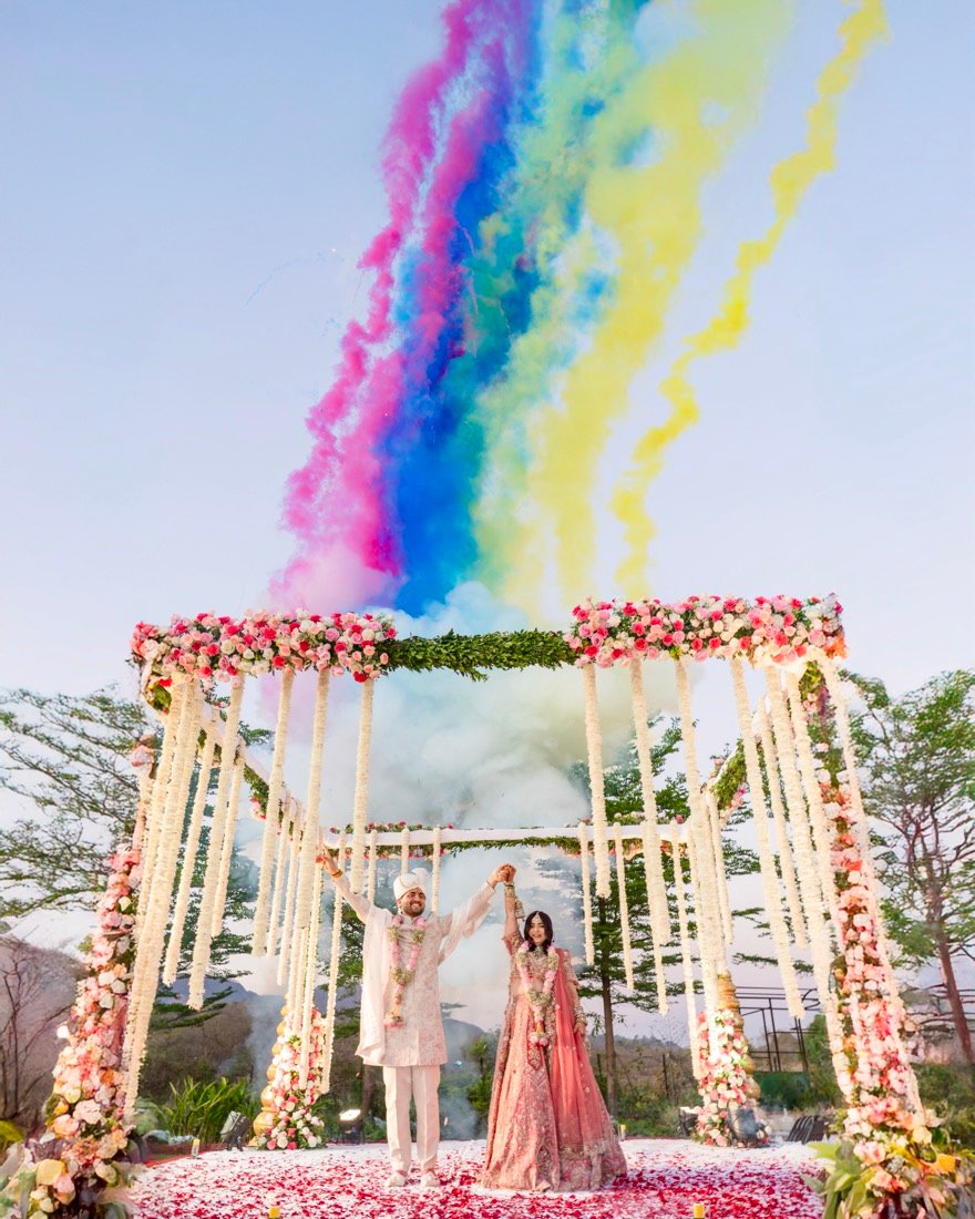 Coloured smoke rising over a floral mandap as the couple stand beneath it