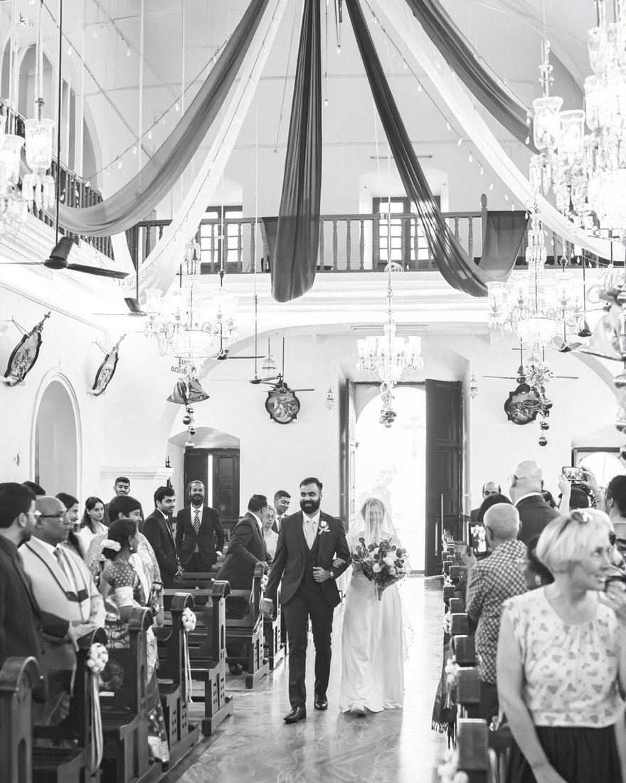 A bride walking down the aisle of a chapel, in black and white