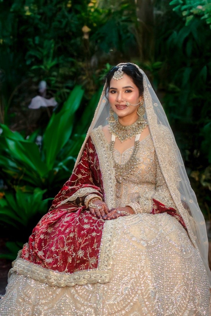A bride in a red and ivory lehenga seated among tropical leaves