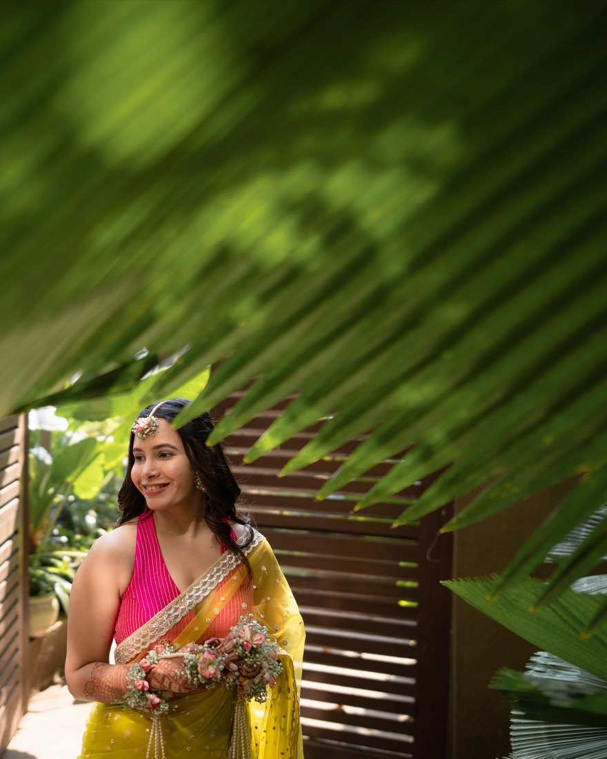 A bride in a yellow sari framed by the shadows of palm leaves