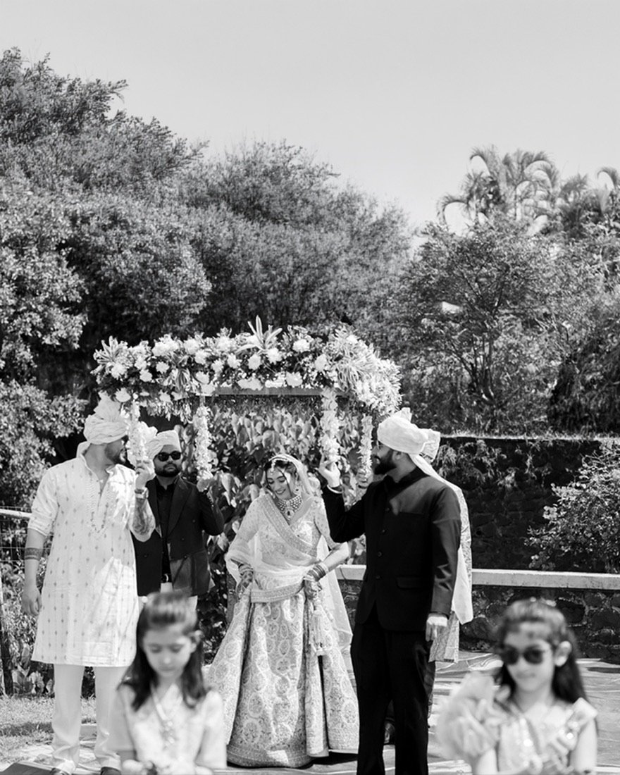 A bride arriving beneath a floral canopy, in black and white